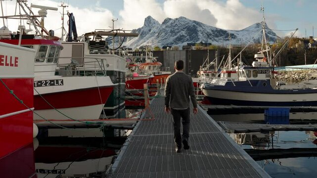 Man walking down docks of a Norwegian Fishing Harbor Town of Hus&oslash;y