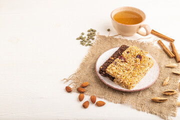 granola bars with caramel, nuts, flakes in ceramic plate on white wooden. Side view, copy space.