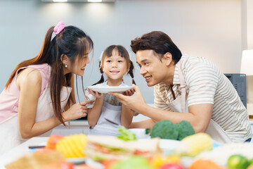 Happy Asian family including father, pregnant mother, and daughter are enjoy preparing and cooking their meal in kitchen together. 