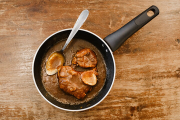Cooked Meat in Pan with Sauce. A close-up view of a frying pan containing cooked meat pieces in a rich, brown sauce, with a metal spoon resting inside the pan. 