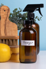 Brown glass bottles of cleaning solutions sit on a white table alongside a sponge, brush, and fresh lemon, creating an organized and inviting cleaning setup. space for text