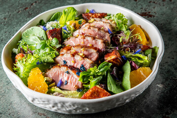 A vibrant salad featuring tender sliced meat atop a mix of fresh greens, colorful flowers, and orange segments, served in a stylish bowl. Perfect for food photography and culinary presentations.
