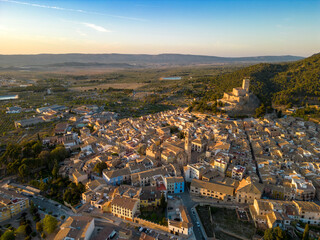 Cinematic aerial view of Biar city, at sunset. Beautiful medieval city. Fortress on top of the hill. Warm sunset colours reflecting on the landscape and castle. Famous travel destination in Spain.