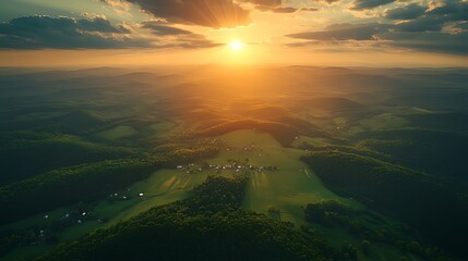 Obraz premium Aerial view of sunset over green hills and village.