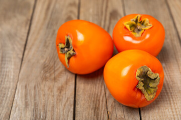 Persimmon on textured wooden background. Persimmon fruit. A piece of ripe, juicy, sweet persimmon fruit. Vegan. Orchard. Close-up. Space for text. Copy space.