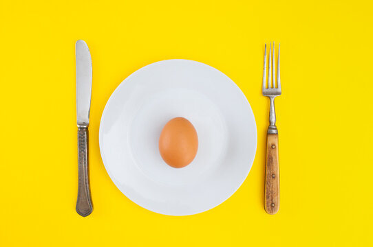 Single egg on plate and  fork and table-knife on a yellow background