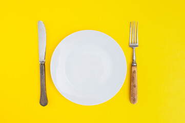Empty plate with antique fork and table-knife on yellow background