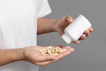 Woman pouring out beige capsules into hand from white plastic bottle closeup over white shirt