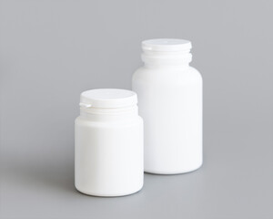 White plastic pill bottles closeup against grey, mockup. Healthcare concept, herbal supplements