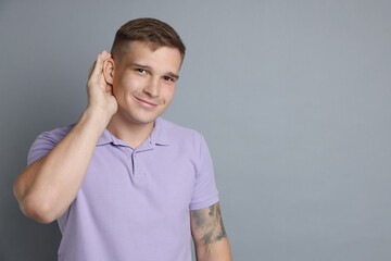 Man showing hand to ear gesture on gray background, space for text