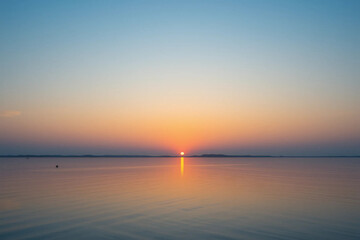 Obraz premium Scenic Gradient Sunset Sky: Deep Orange to Light Blue with Calm Water Reflection and a Clear Horizon