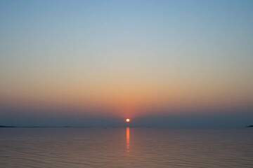 Fototapeta premium Scenic Gradient Sunset Sky: Deep Orange to Light Blue with Calm Water Reflection and a Clear Horizon