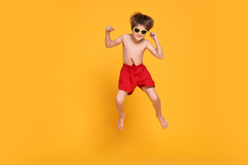 Little boy in beachwear jumping on orange background, space for text © New Africa
