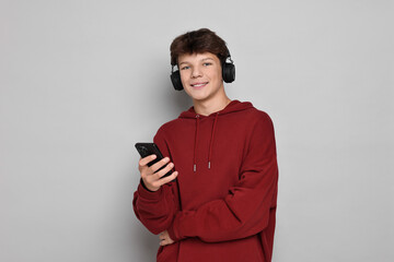 Teenage boy in headphones with smartphone on light grey background, space for text