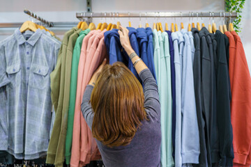 Shopper browsing multicolored hoodies, selecting preferred clothing item in retail environment