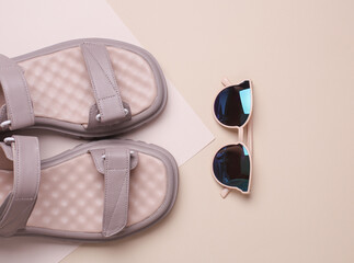 Women's leather sandals with sunglasses on beige background. Summer shoes and accessories. Top view