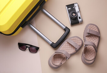 Travel luggage with camera, women's sandals and sunglasses on beige background. Summer Vacation,...