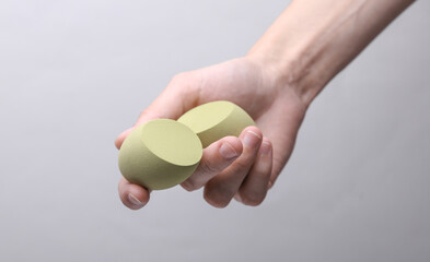 Female hand holding makeup sponges on gray background