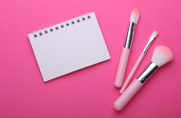 Pink Makeup brushes and notebook on pink background. Beauty blog