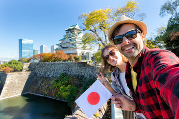 Fototapeta premium A young tourist couple taking a selfie with Japan flag at Osaka Castle, Osaka Castle is one of the most famous landmarks in Japan and Osaka, vacation lifestyle.