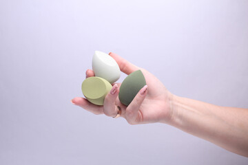Female hand holding makeup sponge on grey background