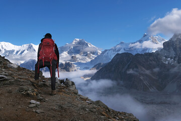 Fototapeta premium Silhouette of hiker with red backpack on mount Gokyo Ri, looking at beautiful panorama of Himalayas. Gokyo, Nepal