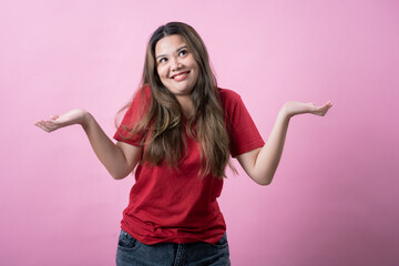 Asian woman in a red shirt with long brown hair shrugs her shoulders with a confused expression,...
