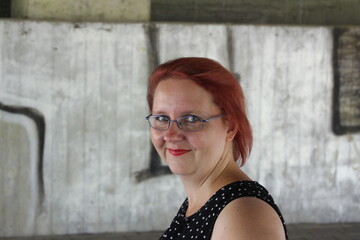 A woman with red hair and glasses is smiling at the camera