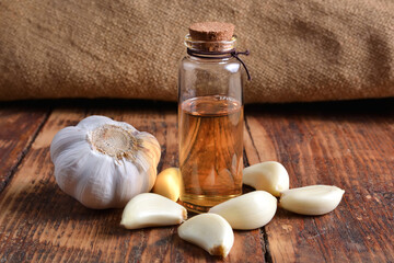 Raw and ripe garlic with garlic oil in a small glass bottle on a wooden table. Organic remedy and natural cleaner concept. Close-up