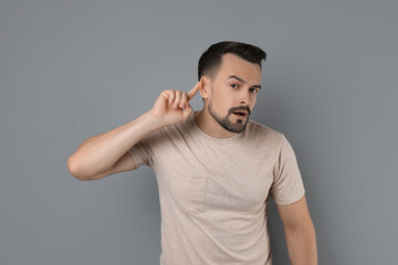 Man showing hand to ear gesture on grey background