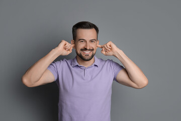 Fototapeta premium Man covering his ears with fingers on grey background