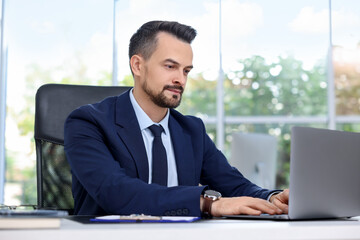 Handsome banker working with laptop at table in office