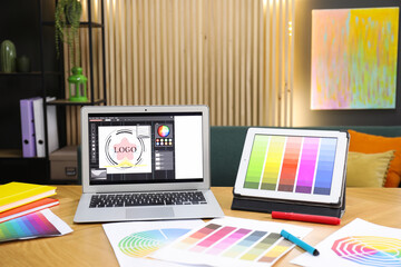 Designer's workplace with laptop, tablet, stationery and palettes on wooden table indoors