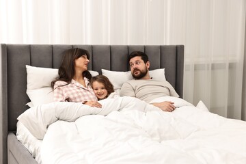 Fototapeta premium Happy playful daughter with her overwhelmed parents in bed at home