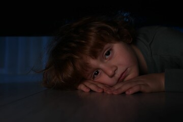 Fearful boy hiding under bed at night