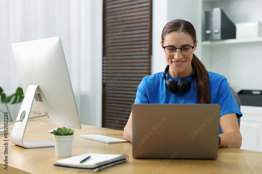 Poster programmer working on laptop and computer at wooden desk indoors