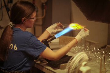 A young girl blows glass toys for the Christmas tree. Glass blower at a Christmas tree decorations factory. Fire and glass..