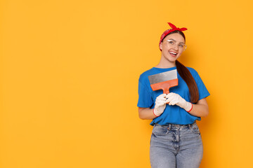 Portrait of young decorator with putty knife on orange background, space for text