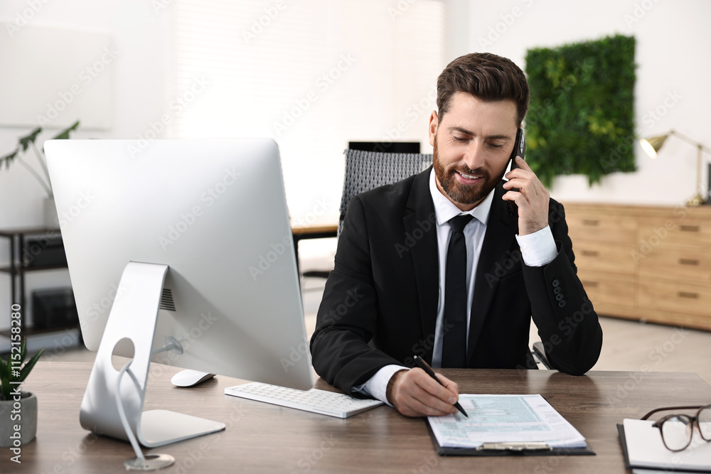 Poster man talking on smartphone while working at table in office