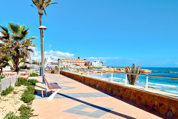 Picturesque view of Torre de la Horadada, charming coastal town in southern Alicante province, Costa Blanca, Spain. Serene promenade with bench, palm trees, and stunning Mediterranean Sea view