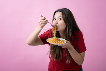 Asian woman in a red shirt with long brown hair eagerly eating noodles from a white plate with a...