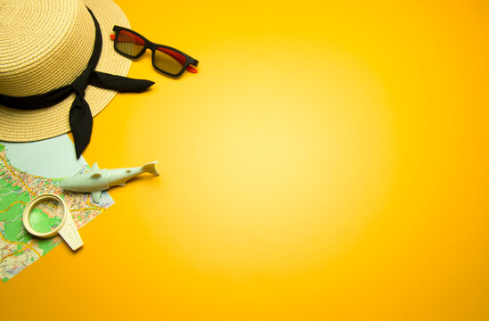 Straw hat, map, shark, sunglasses and magnifying glass on yellow sunny background. Summer holiday, vacation.Travel concept. Top view.Space for text.