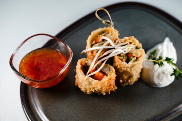 fried crispy spring rolls stuffed with vegetables, topped with sprouted wheat, served on dark clay plate with yoghurt and sweet chili sauce