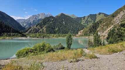 A beautiful scene unfolds with majestic mountains rising high into the sky, their peaks dusted with snow. Nestled at the base of these towering giants are tranquil lakes, their crystal-clear waters re