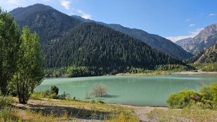 A beautiful scene unfolds with majestic mountains rising high into the sky, their peaks dusted with snow. Nestled at the base of these towering giants are tranquil lakes, their crystal-clear waters re