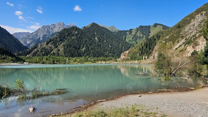 A beautiful scene unfolds with majestic mountains rising high into the sky, their peaks dusted with snow. Nestled at the base of these towering giants are tranquil lakes, their crystal-clear waters re