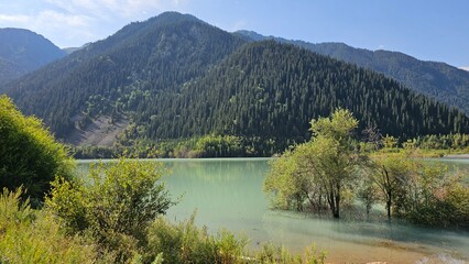 A beautiful scene unfolds with majestic mountains rising high into the sky, their peaks dusted with snow. Nestled at the base of these towering giants are tranquil lakes, their crystal-clear waters re