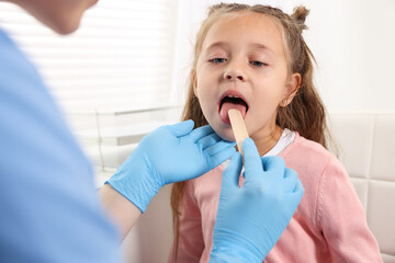 Doctor examining girl's throat with tongue depressor in clinic © New Africa