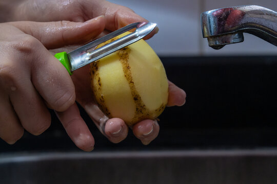 Potapo peeling. Hands peeling raw potato with vegetable peeler in the kitchen.