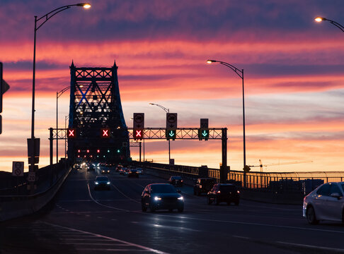 view of a suspended metal bridge on a colourful sunset with cars driving down